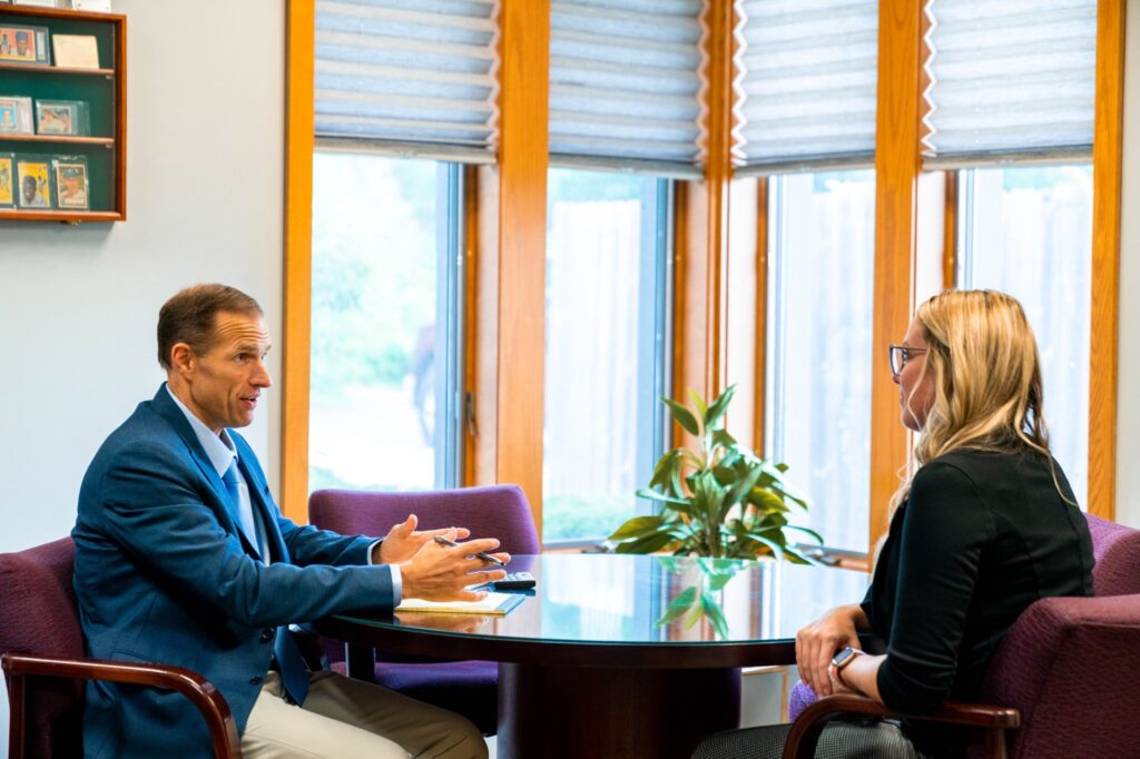 A retirement financial planner sits down with a new client at a wooden table.