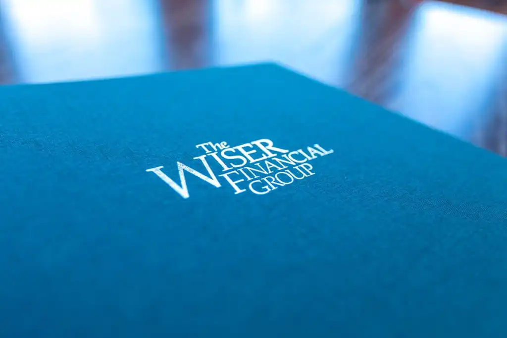 A closeup view of a Wiser Financial Group branded folder lying on a wooden desk.