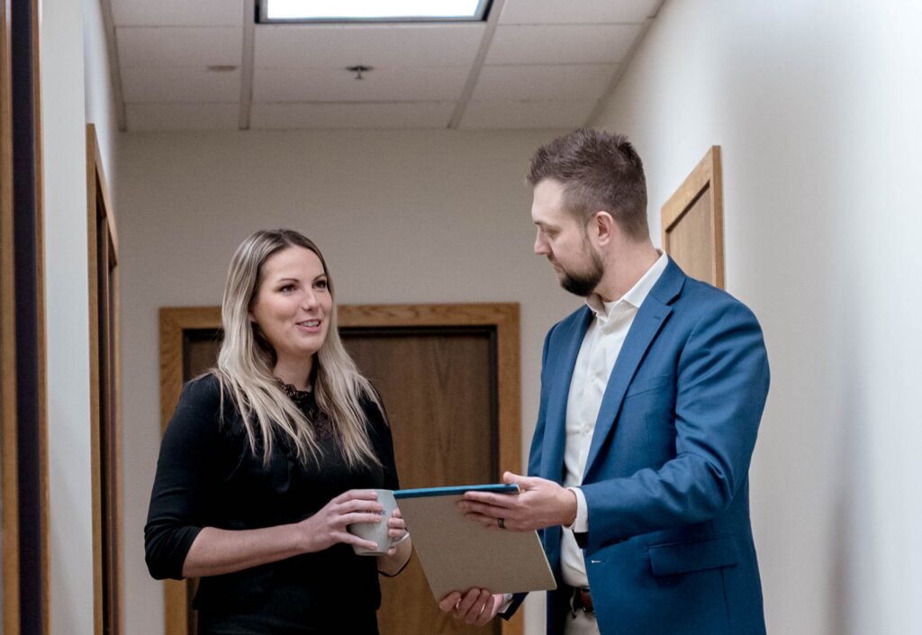 A business man and woman discuss paperwork in an office hallway.