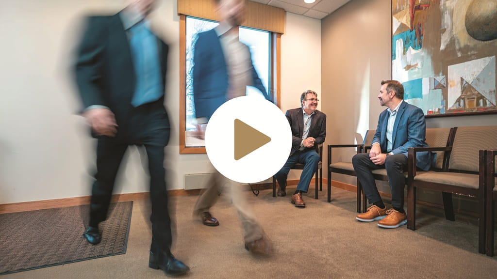 A photo of members of Wiser Financial Group's team talking in a lobby, with a video play button overlay in the center of the photo.